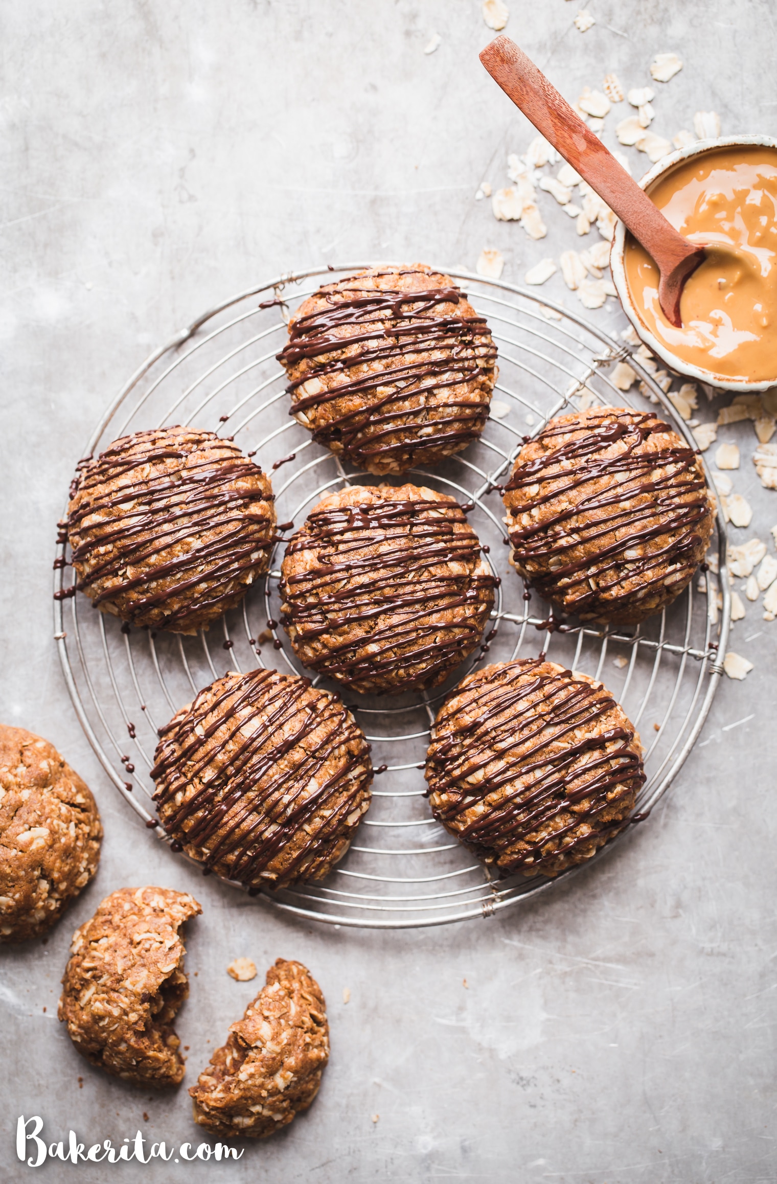 Close up of peanut butter oatmeal cookies, drizzled with dark chocolate, with bowl of peanut butter in the corner.