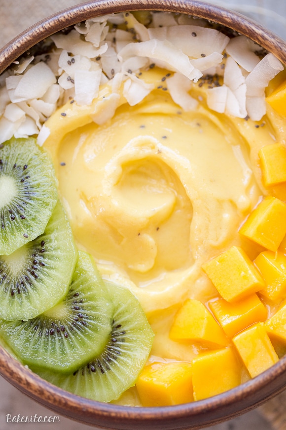 Close up on Mango Pineapple Smoothie Bowl with coconut on top, kiwi on the left side, mango chunks on the right.
