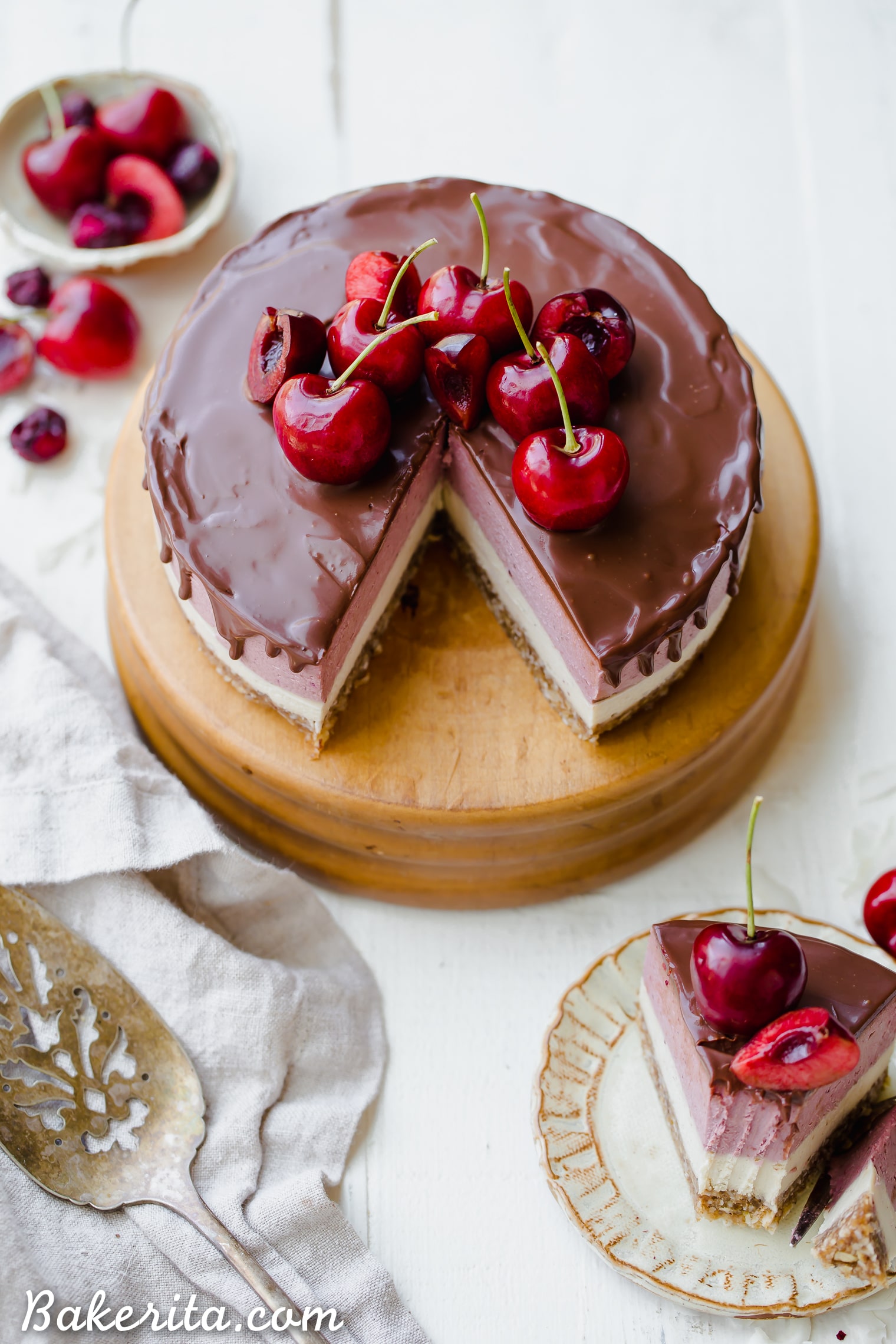 This No Bake Cherry Cheesecake has a pecan coconut crust, a layer of creamy vanilla bean cheesecake, topped by a layer of vibrant cherry cheesecake. Vegan dark chocolate ganache is spread all over the top! You'll go crazy for this gluten-free, paleo, and vegan treat.