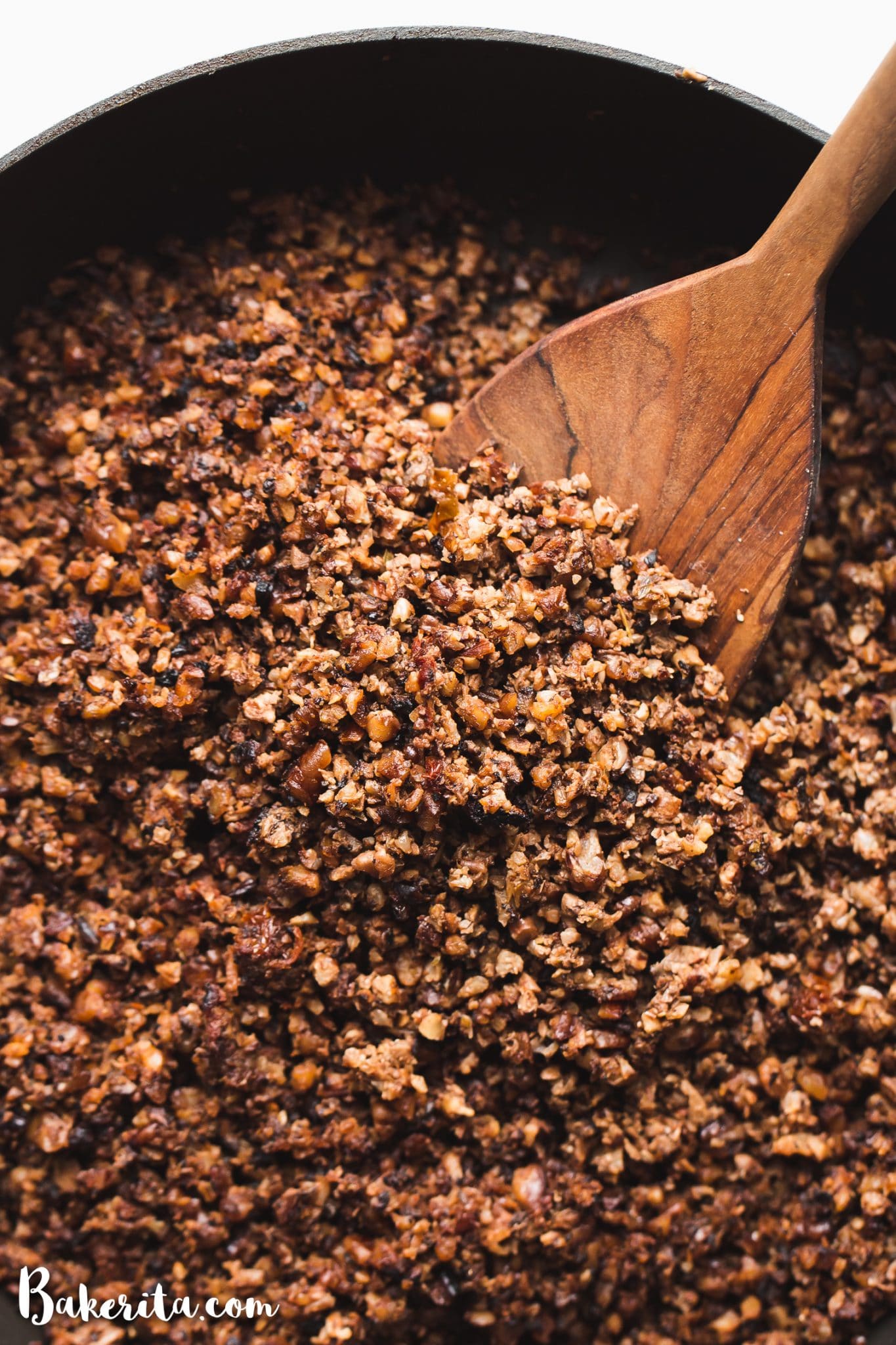 This Vegan Taco Meat recipe is a game-changer! It's made with cauliflower, mushrooms, nuts, and spices. Vegan ground meat filling is in a black cast iron pan with a wooden spoon.