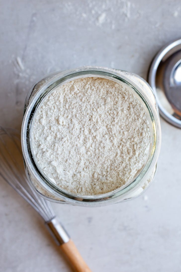 Gluten-Free Bread Flour Blend in a large mason jar with a whisk in the foreground and the silver lid in the background, shot from overhead.