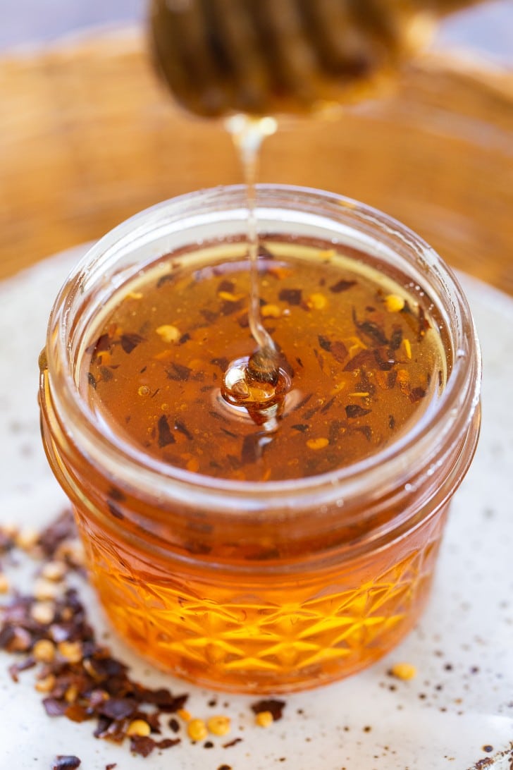 Jar of honey with chili flakes mixed in, in a mason jar on a white plate.